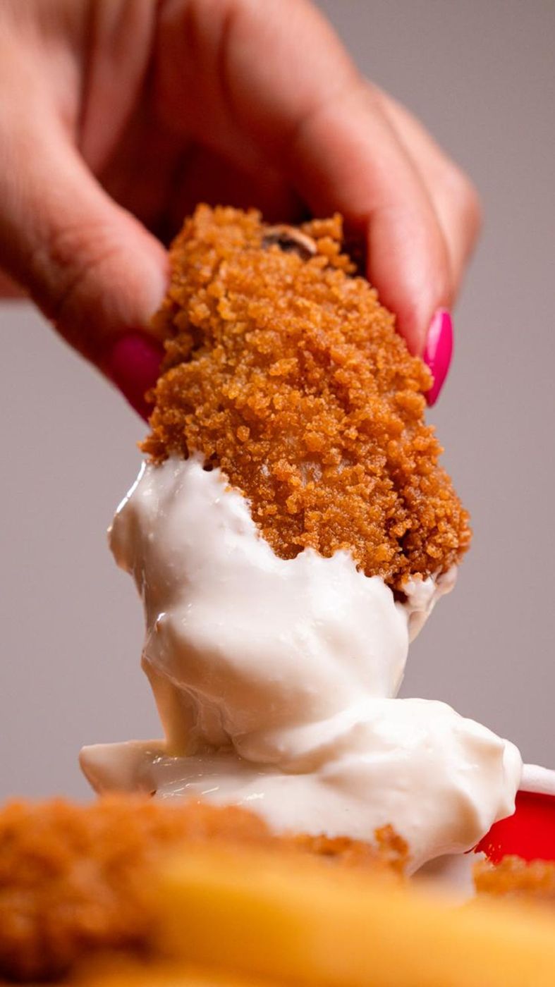 Pedaço de frango frito sendo mergulhado no molho da casa